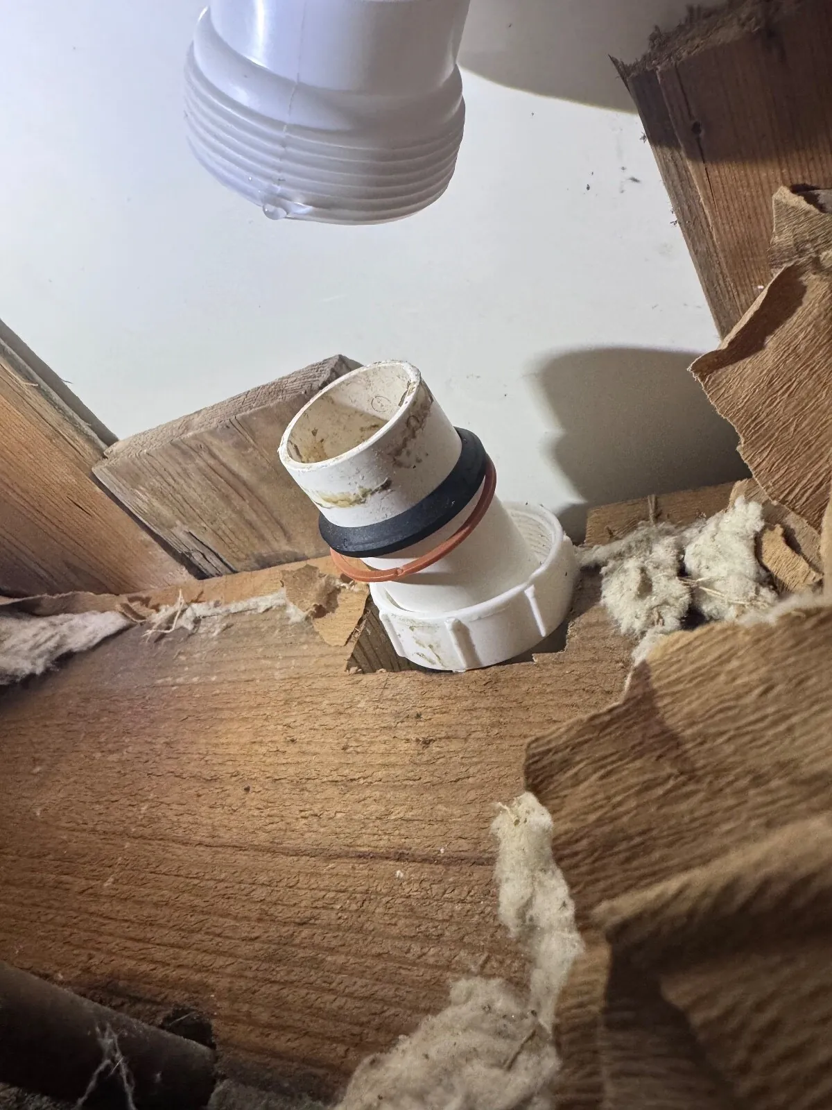 White plastic waste pipe end tilted out of its nut in a joist void, with a black and an orange sealing ring on it
